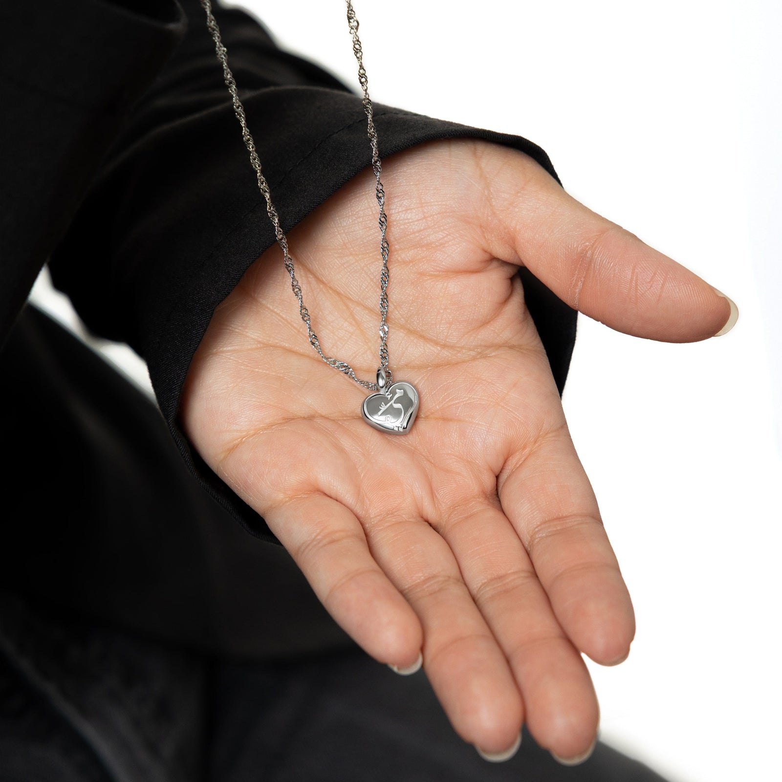 Photo of the silver Mama Heart Charm linked on a silver chain resting on the palm of the model's hand.