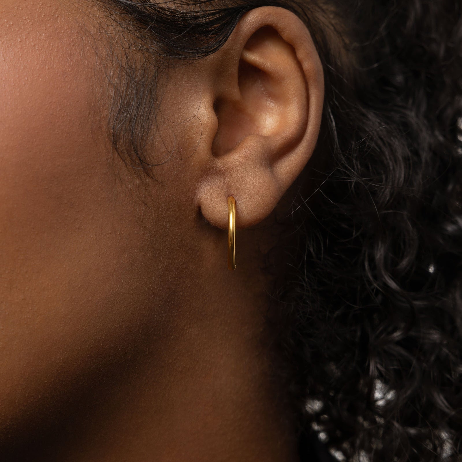 Close up of the gold Medium Essential Hoops | 16mm as worn by the model on their left ear.