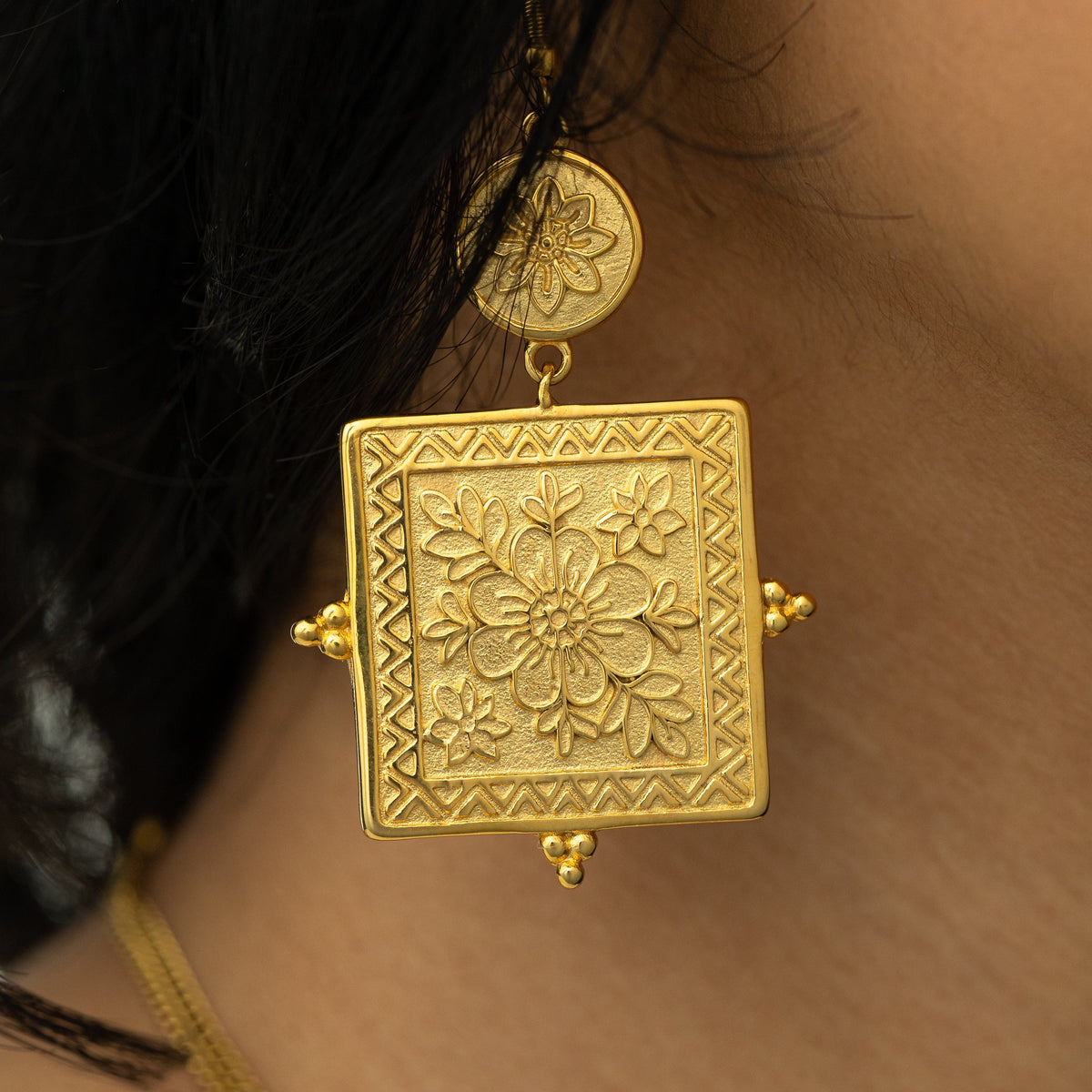 Close-up of the gold Mehndi Floral Earring worn on ear, showing detailed floral engraving on the square pendant.