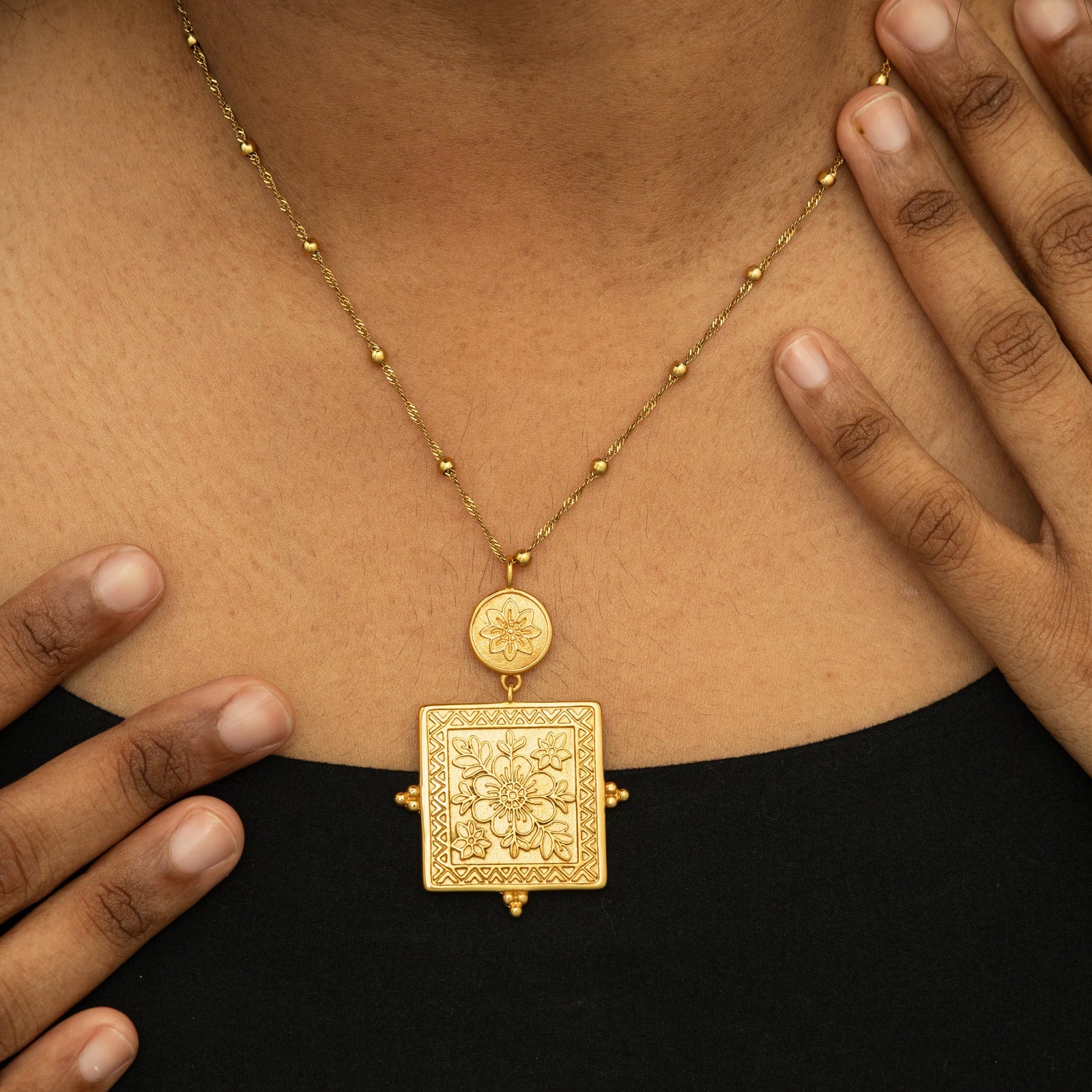 Close-up of the Mehndi Floral Necklace resting against the chest, featuring a gold floral square pendant and round charm on a beaded chain.