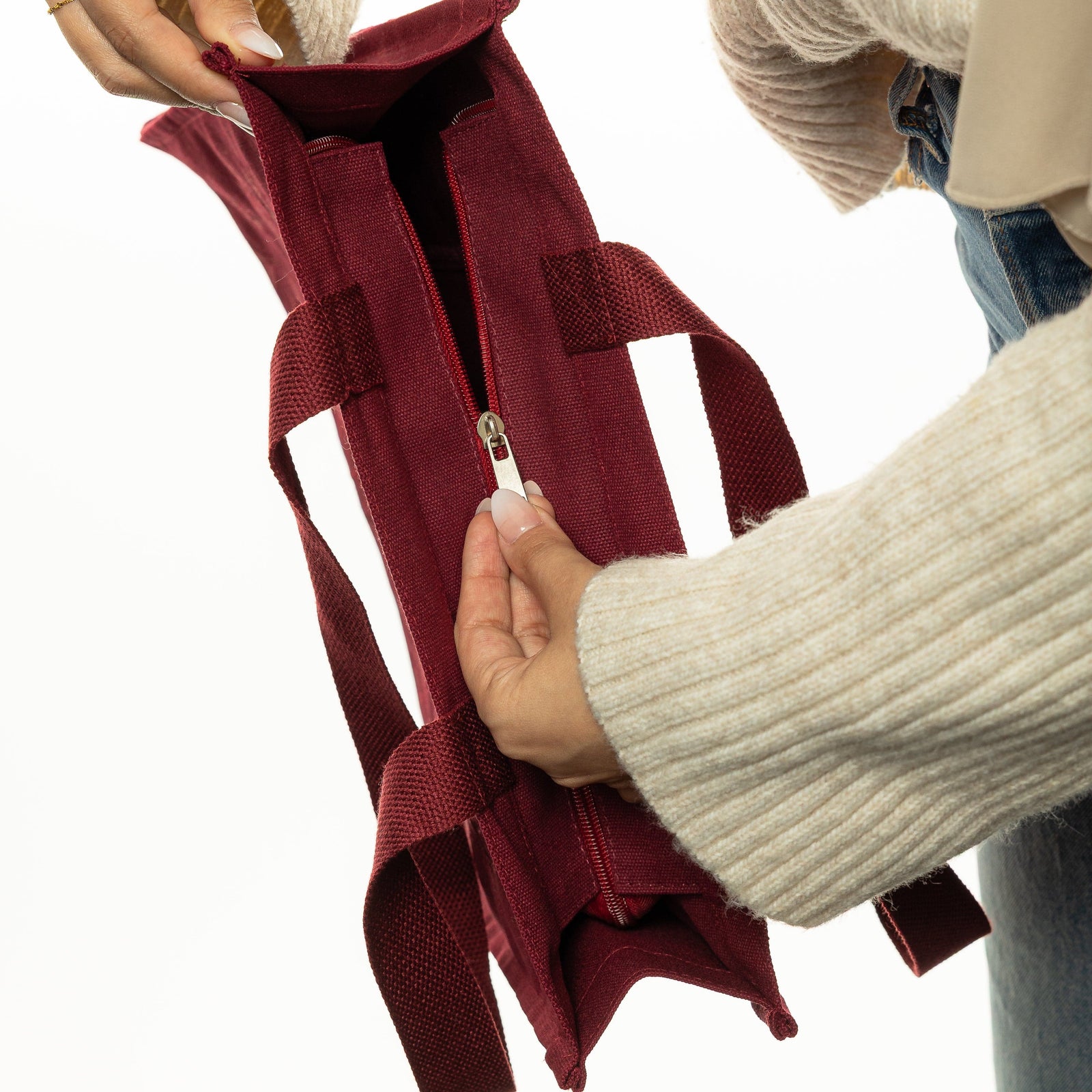 Close up photo showing the model adjusting the main zipper of the maroon bag.