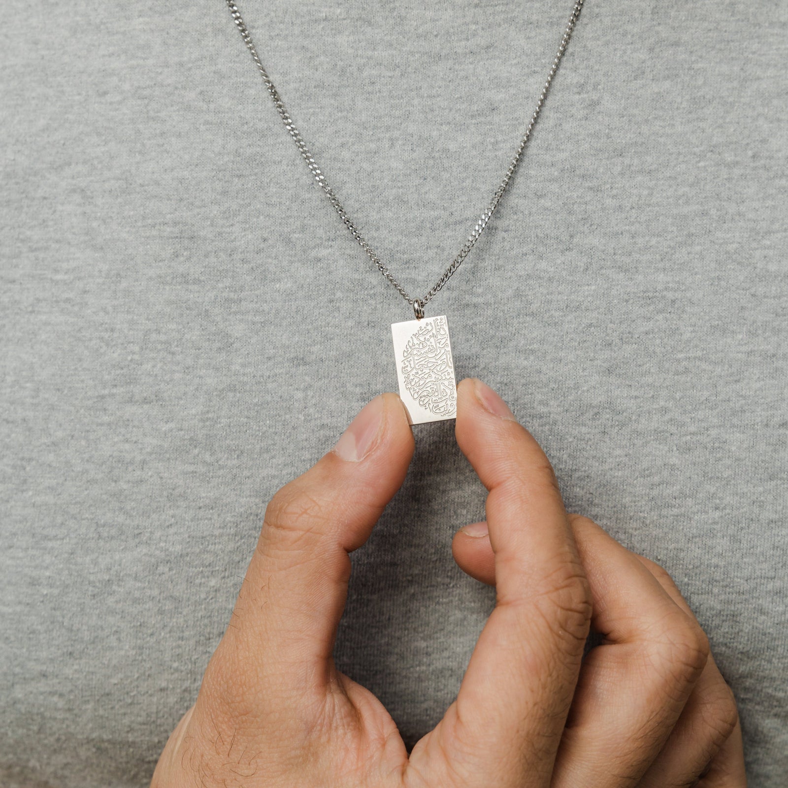 Close up of the silver "Tranquility in Them" Necklace as the model holds the pendant between their fingers.