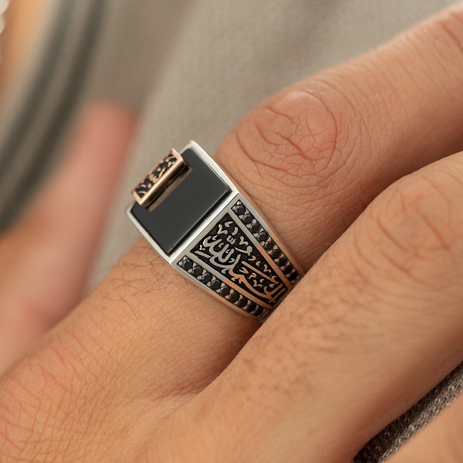 Man wearing a silver ring with a black onyx stone and an Arabic calligraphy plate reading ‘Bismillah, Alhamdulillah,’ styled with black side stones.