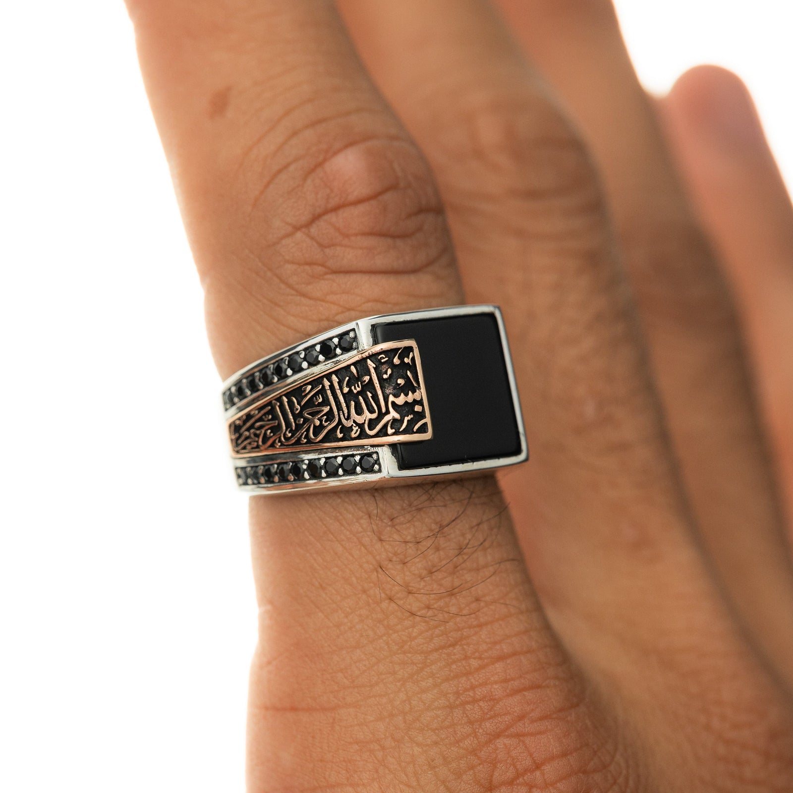 Silver men’s ring with a black onyx stone and rose-gold Arabic calligraphy reading ‘Bismillah, Alhamdulillah,’ shown on a man’s hand.