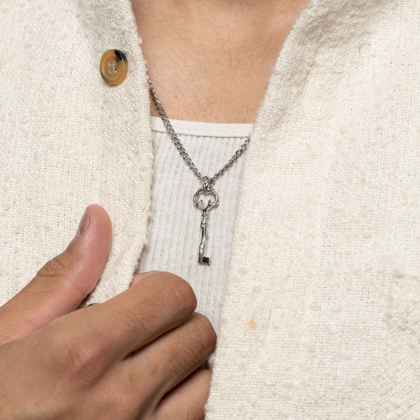 Man wearing the Palestine Key of Return Necklace layered over a ribbed white tank and cream overshirt.