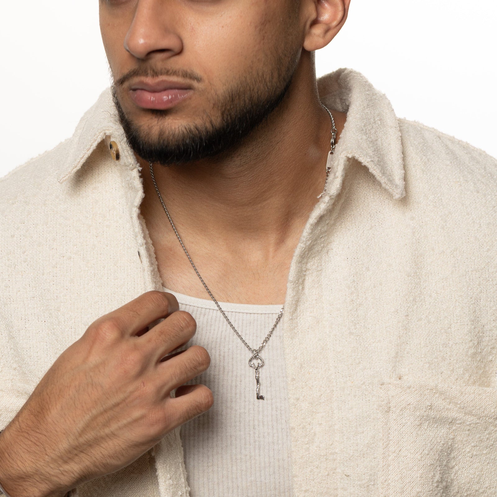 Man wearing the Palestine Key of Return Necklace layered over a ribbed white tank and cream overshirt.