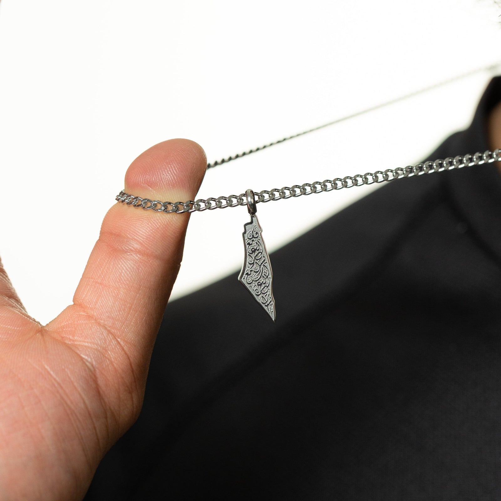 Thumb pulling the chain of a silver With Hardship Comes Ease Map necklace 