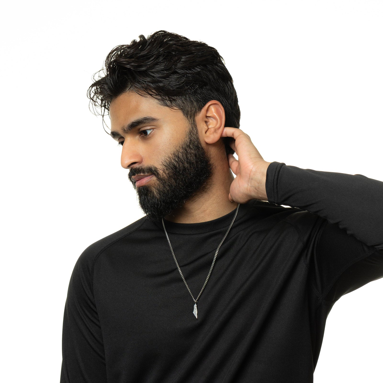 Man wearing a black shirt and a silver With Hardship Comes Ease Map necklace, hand on the nape, shot against a white background