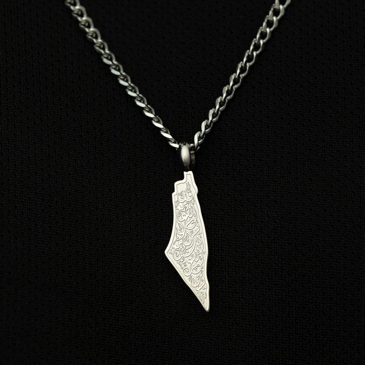 Silver necklace with a map-shaped pendant with arabic calligraphy engraved, shot on a black background