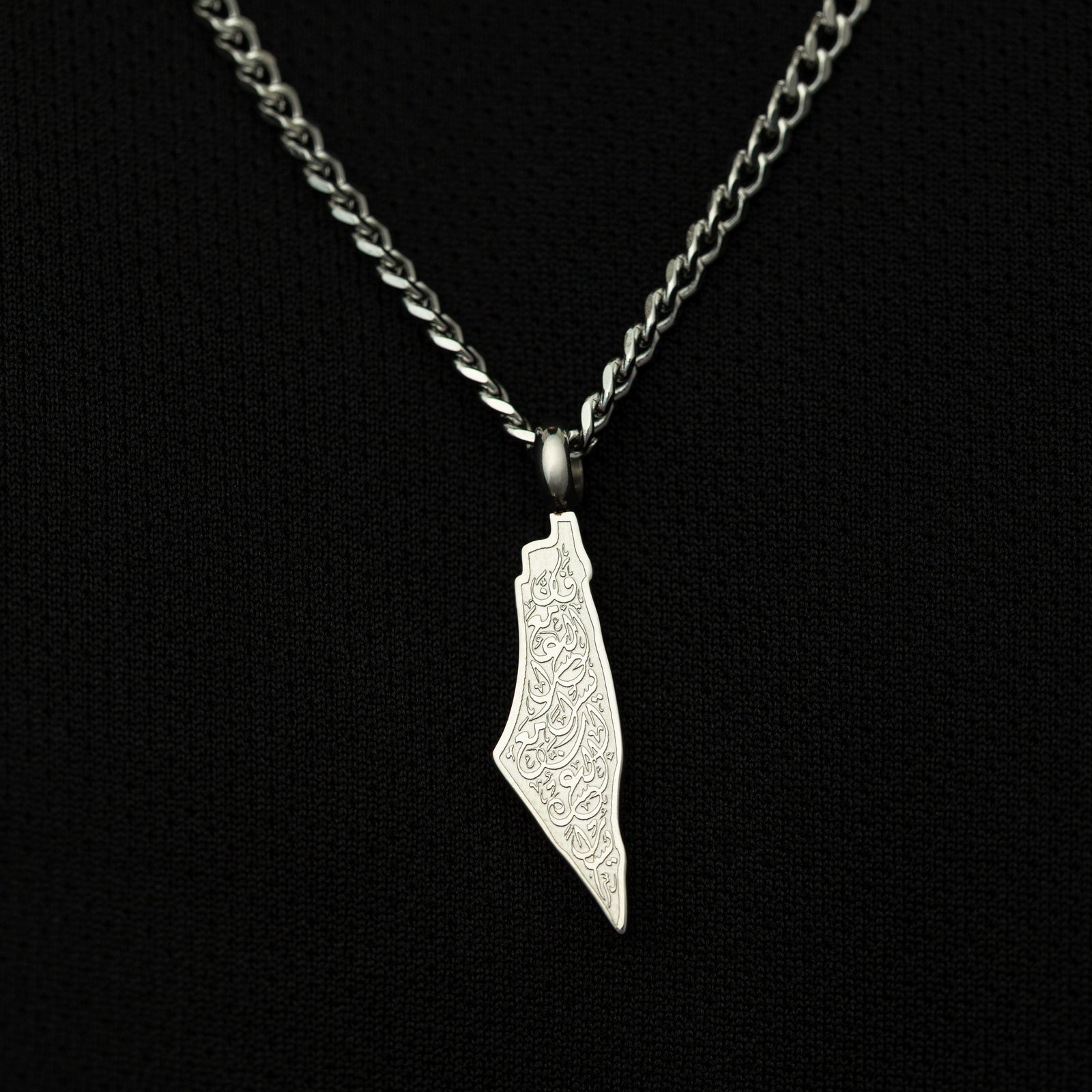 Silver necklace with a map-shaped pendant with arabic calligraphy engraved, shot on a black background