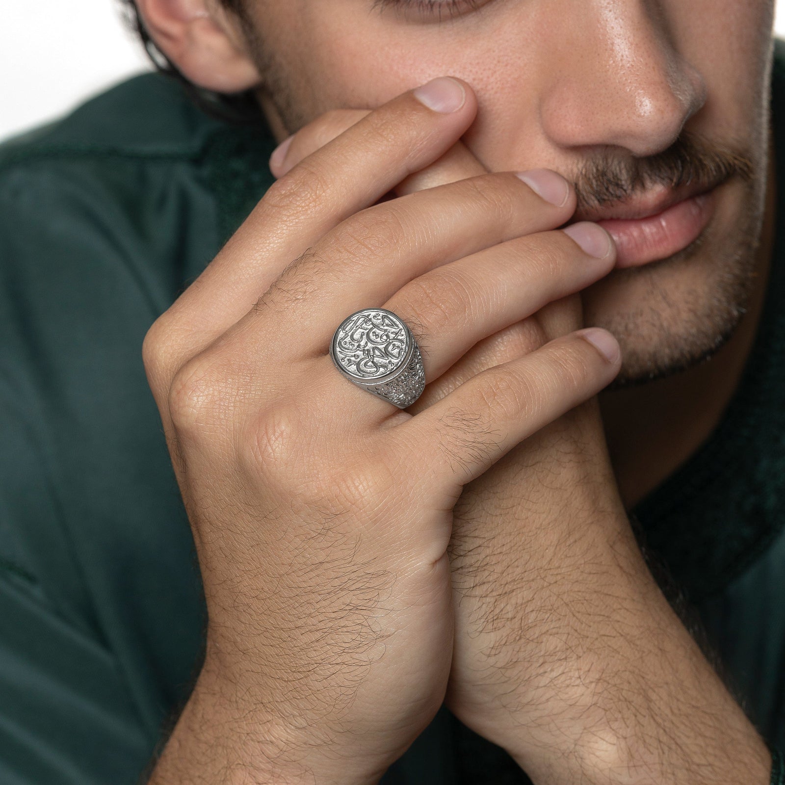 Model's hands are clasped against their face. The model is wearing the silver "Ya Rahman, Ya Raheem" Ring on their right ring finger.