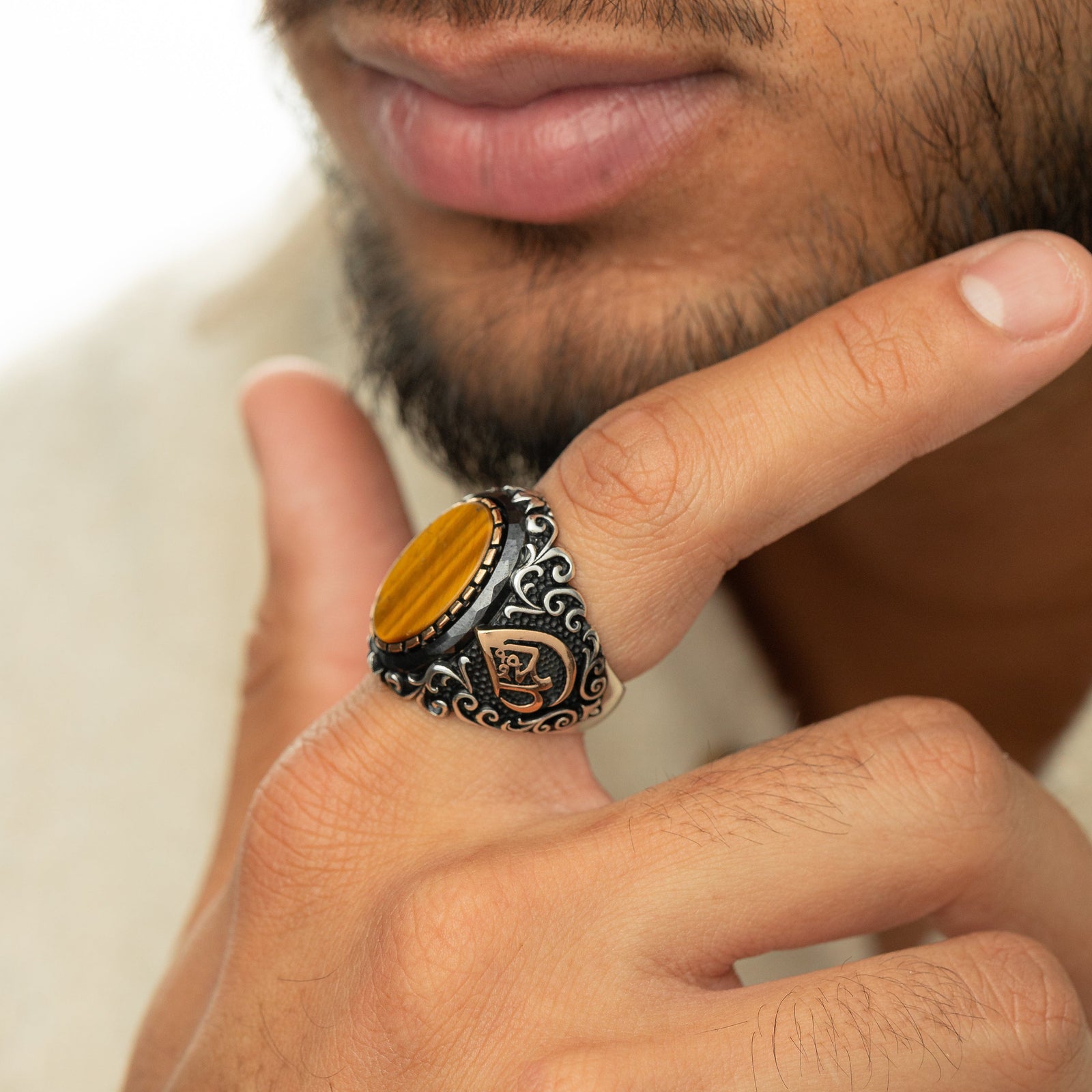 Men’s silver ring with a tiger's eye stone and a gold Arabic calligraphy detail of the word ‘Allah,’ surrounded by ornate black and silver engravings.