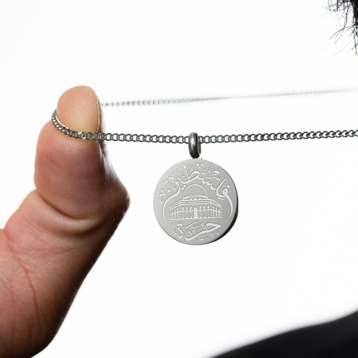 Silver Al-Aqsa ‘Free Palestine’ Necklace held by a hand against a white background