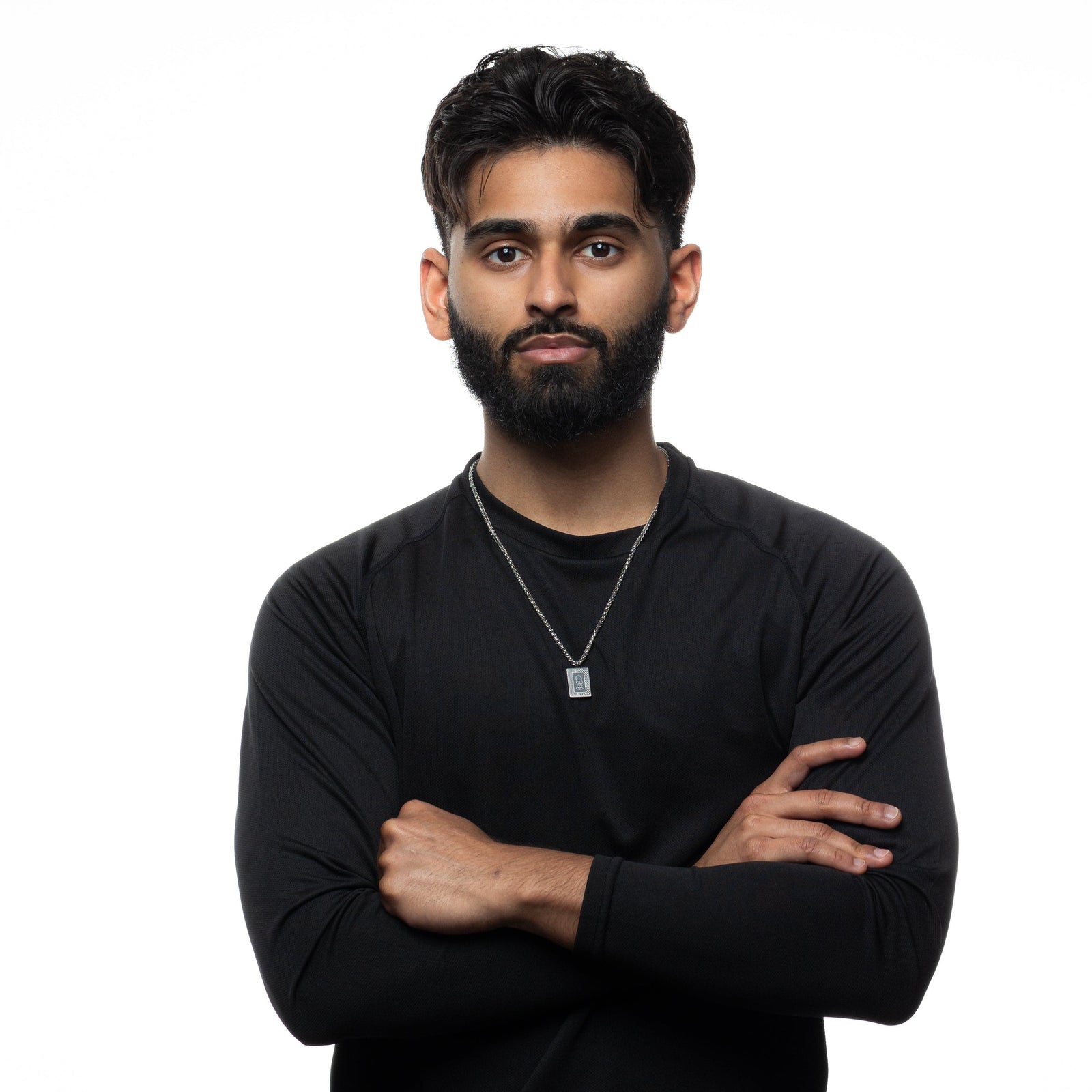 Man wearing a black long-sleeve shirt and silver Handala Necklace with arms crossed on a white background