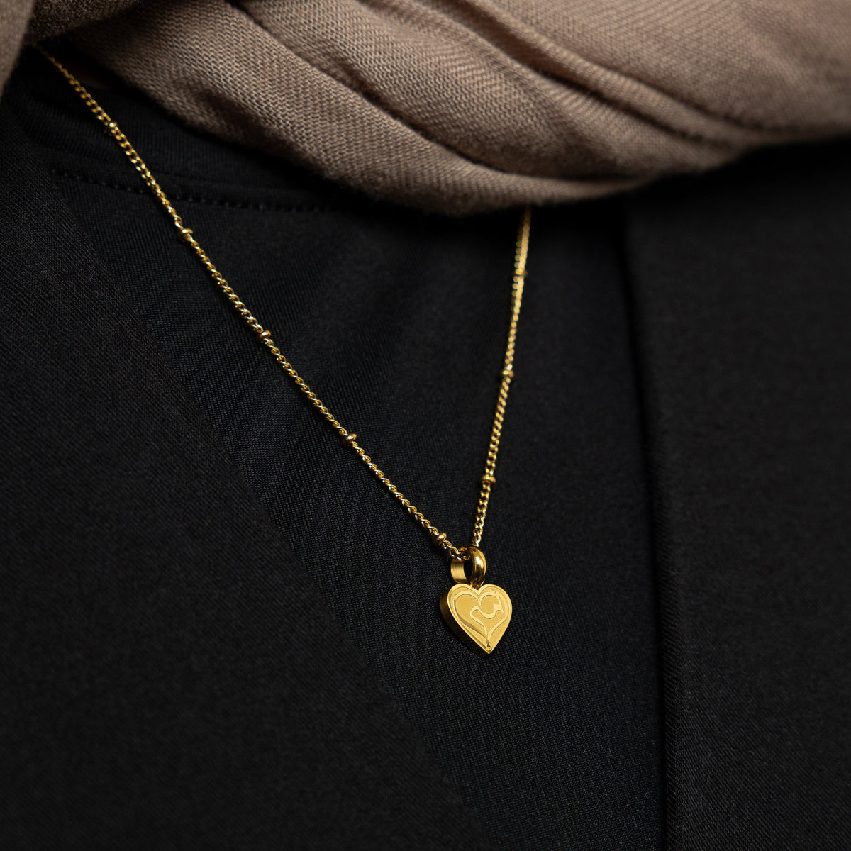 Close up of the gold Mother Love Necklace against the black fabric of the model's shirt.