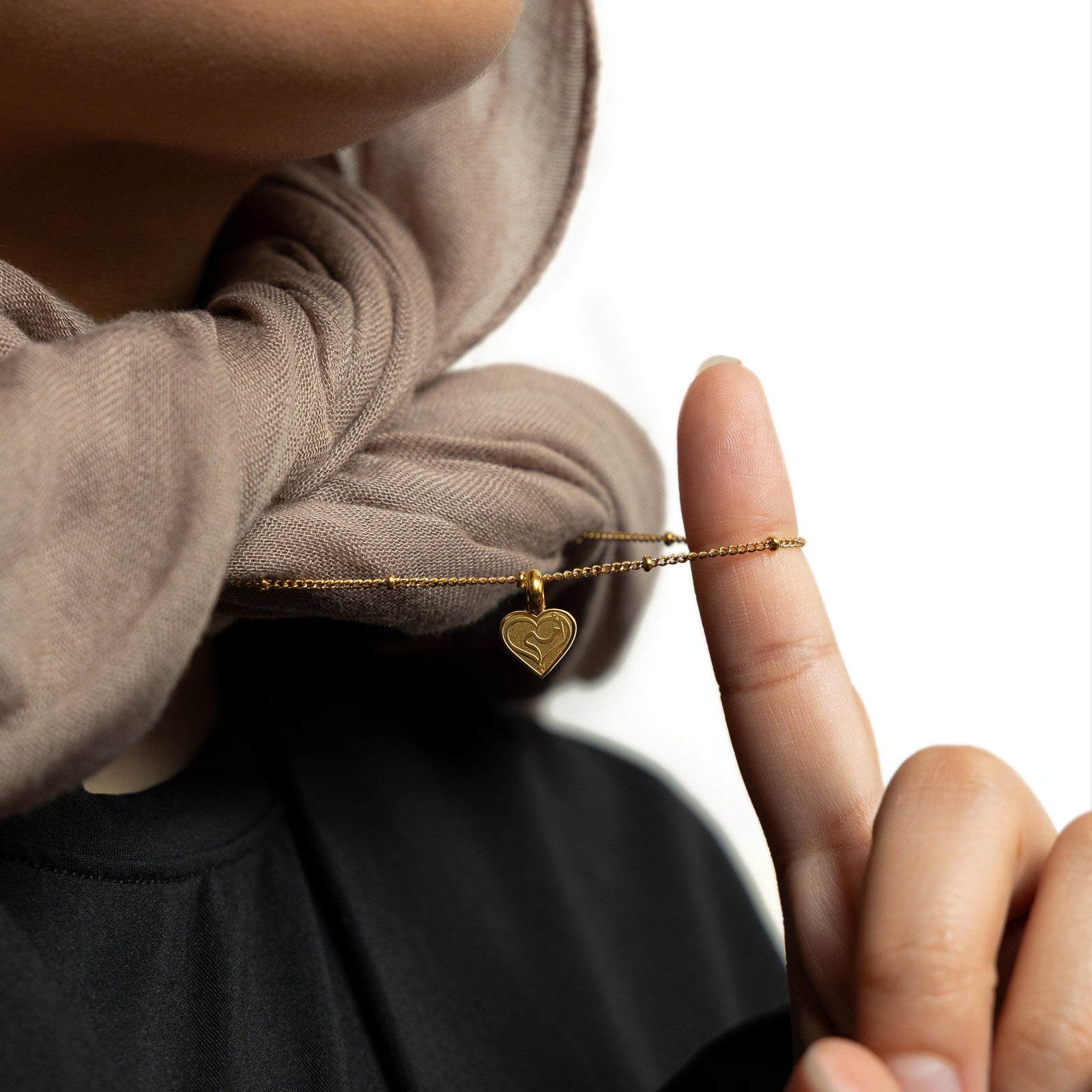 Close up of the gold Mother Love Necklace as the model lifts its chain to show the pendant.