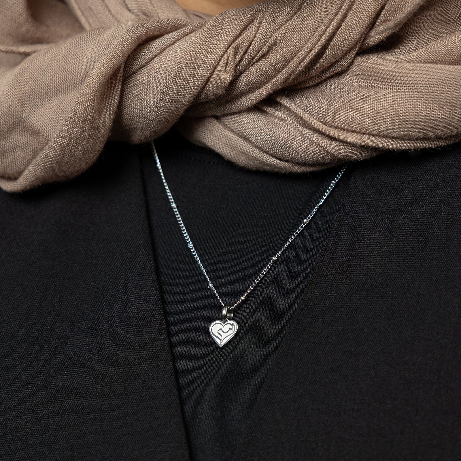 Close up of the silver Mother Love Necklace against the black fabric of the model's shirt.