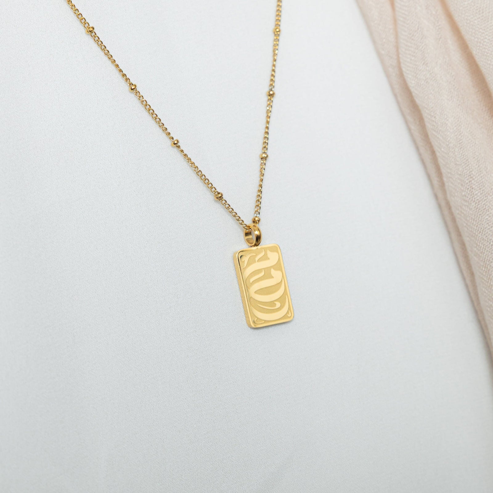 Close up of the gold My Mother Tag Necklace resting against the white fabric of the model's shirt.