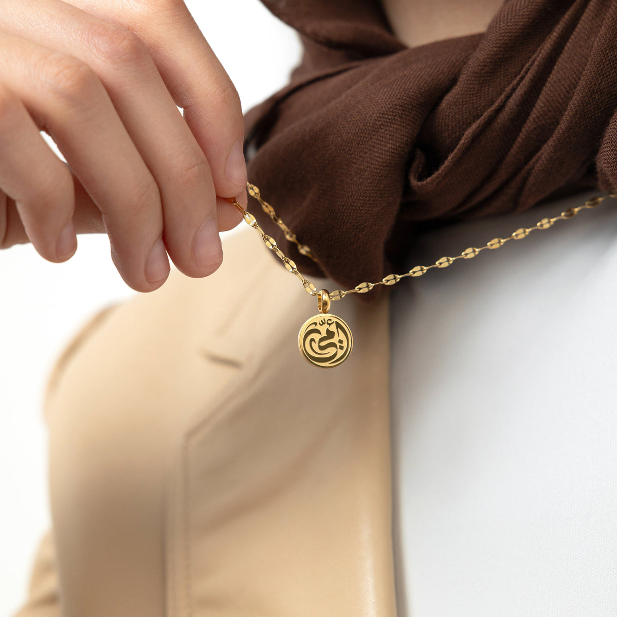 A model wearing the 18K gold-plated My Mother Necklace. The pendant rests gracefully on her collarbone, highlighting the intricate Arabic calligraphy against a neutral-toned outfit.