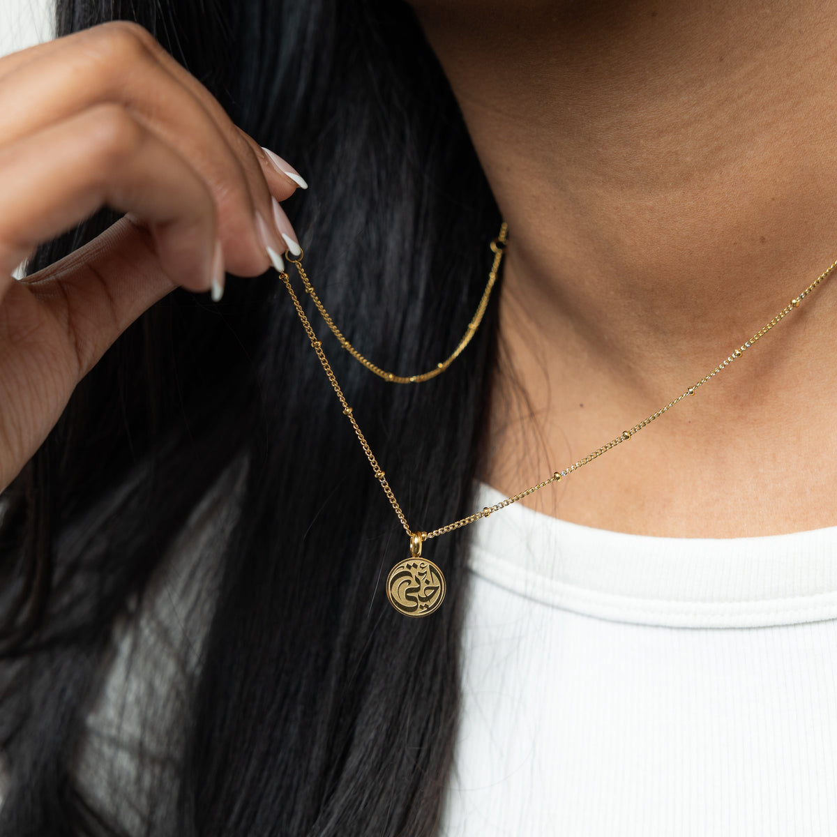 Close up of the gold My Sister Necklace as the model pulls the chain to show its pedant.