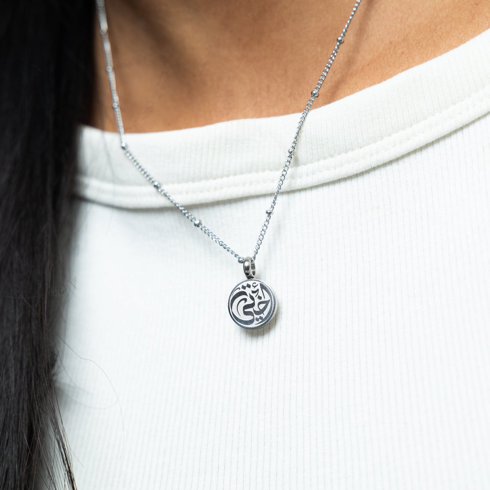 Close up of the silver My Sister Necklace against the white fabric of the model's shirt.