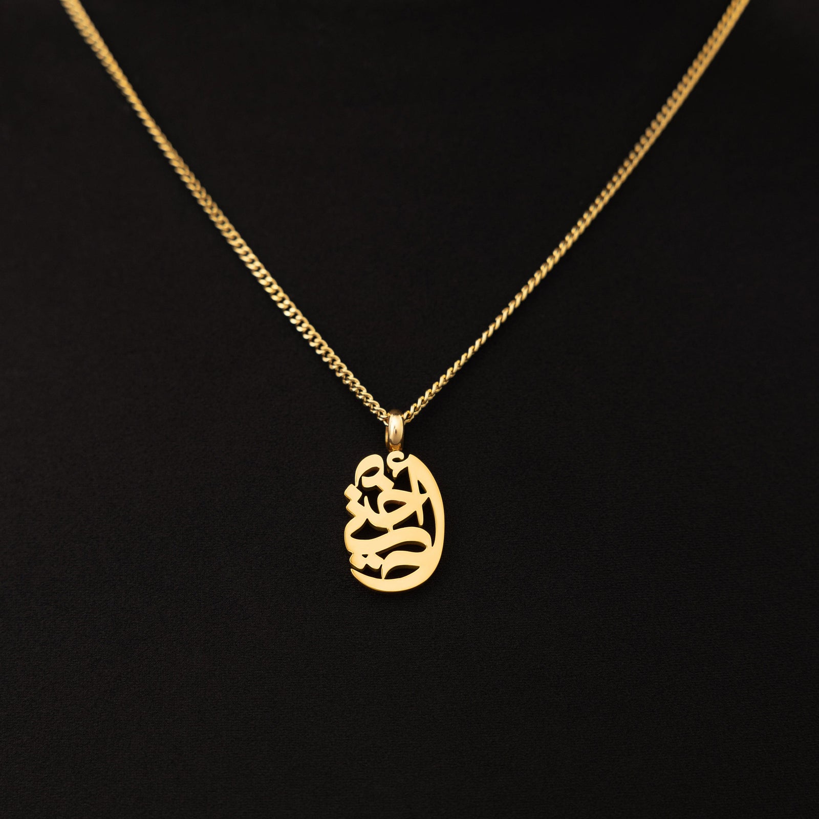 A model wearing the 18K gold-plated My Sister Oval Necklace. The pendant rests gracefully on her collarbone, highlighting the intricate Arabic calligraphy against a neutral-toned outfit.