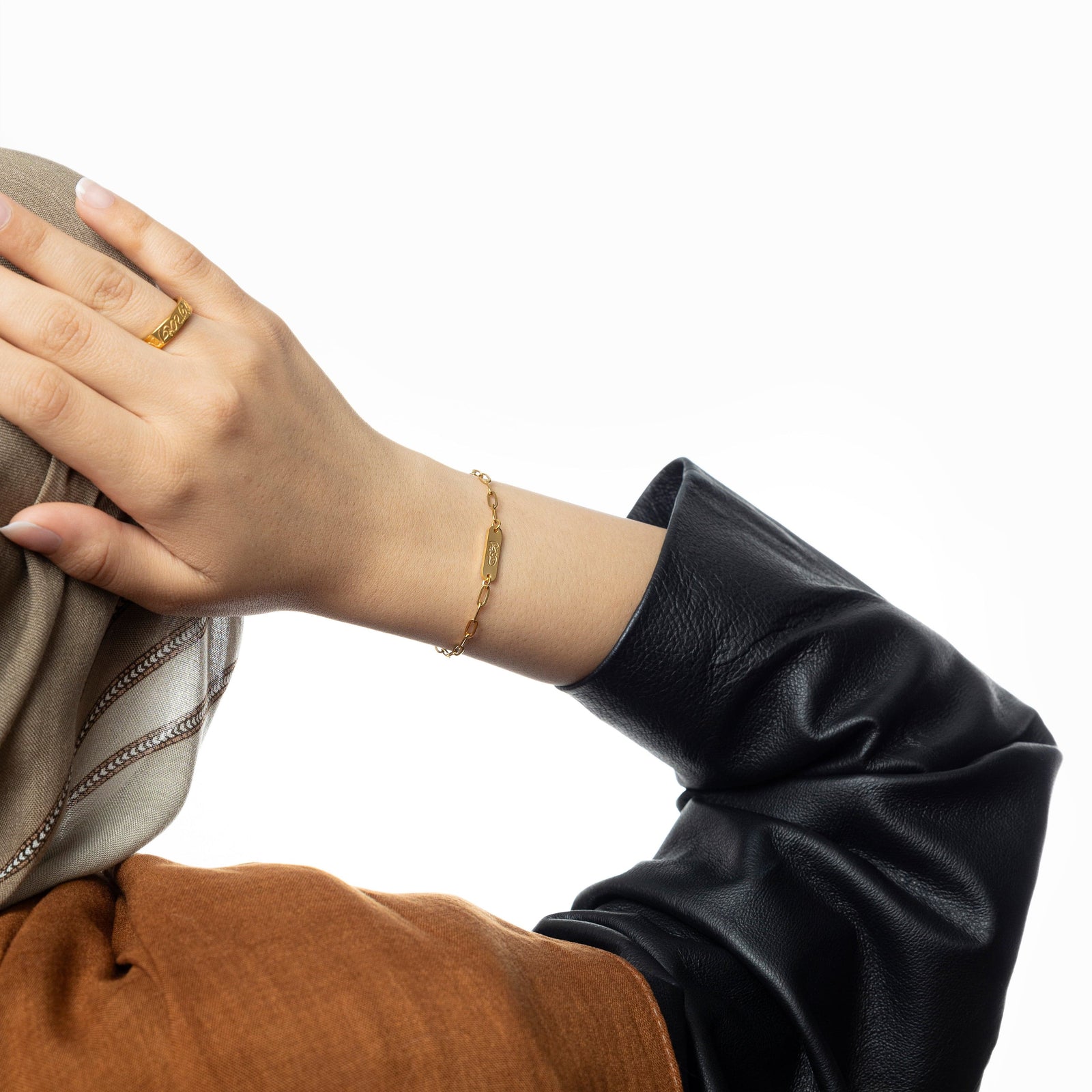 Woman’s arm extended backward showing gold "Ukhti" bracelet paired with a modest outfit and gold ring.