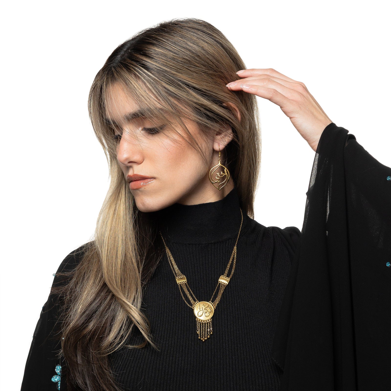 Model touches their hair with their left fingers. The model is wearing the gold "My Sister" Droplet Earrings and a gold necklace.