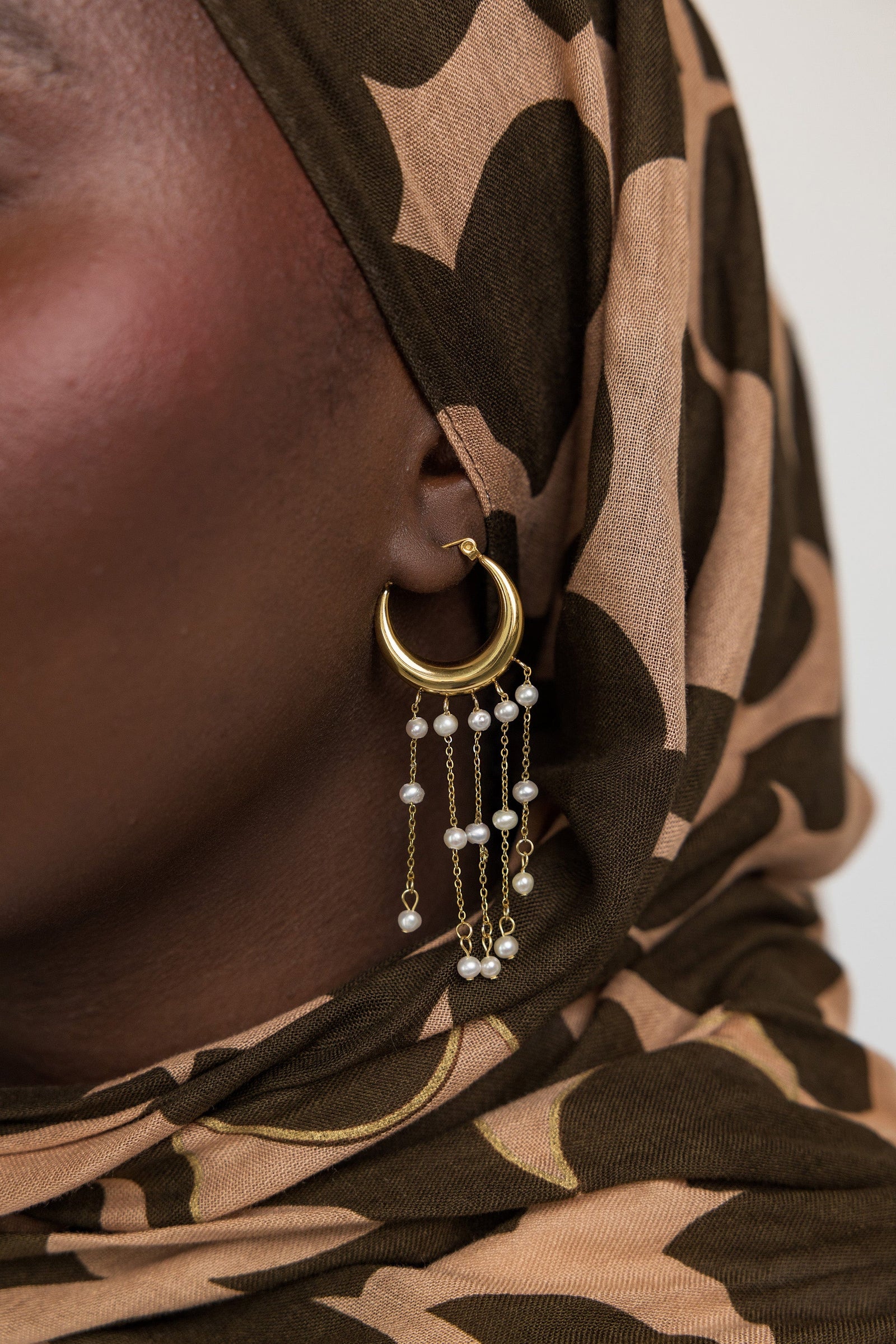 Close up of the gold Raining Pearl Hoop earring as worn by the model on their left ear. 