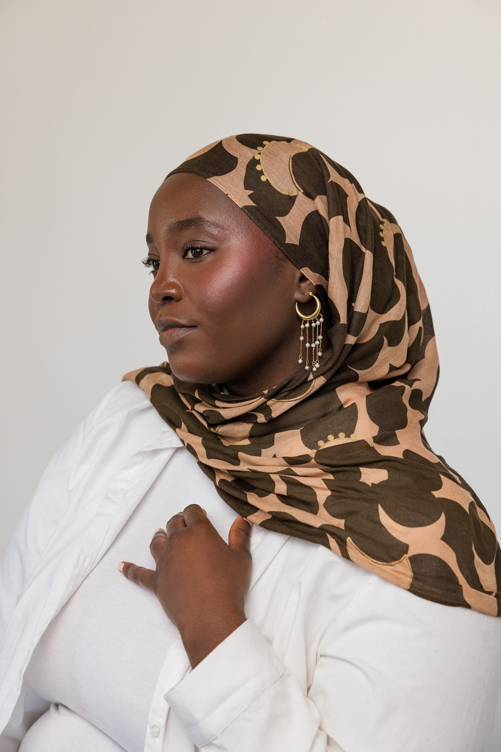 Photo of the model looking away from the camera. The model is angled on their left side profile to show the gold Raining Pearl Hoop earring they are wearing on their left ear.