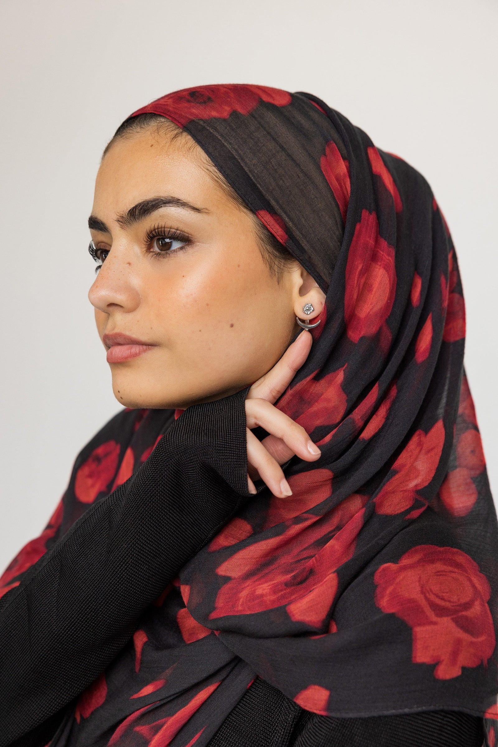 Photo of the model's left side profile. The model is pointing to the silver Damask Rose & Crescent Jacket Earrings | VELA x Nominal they are wearing on their left ear.