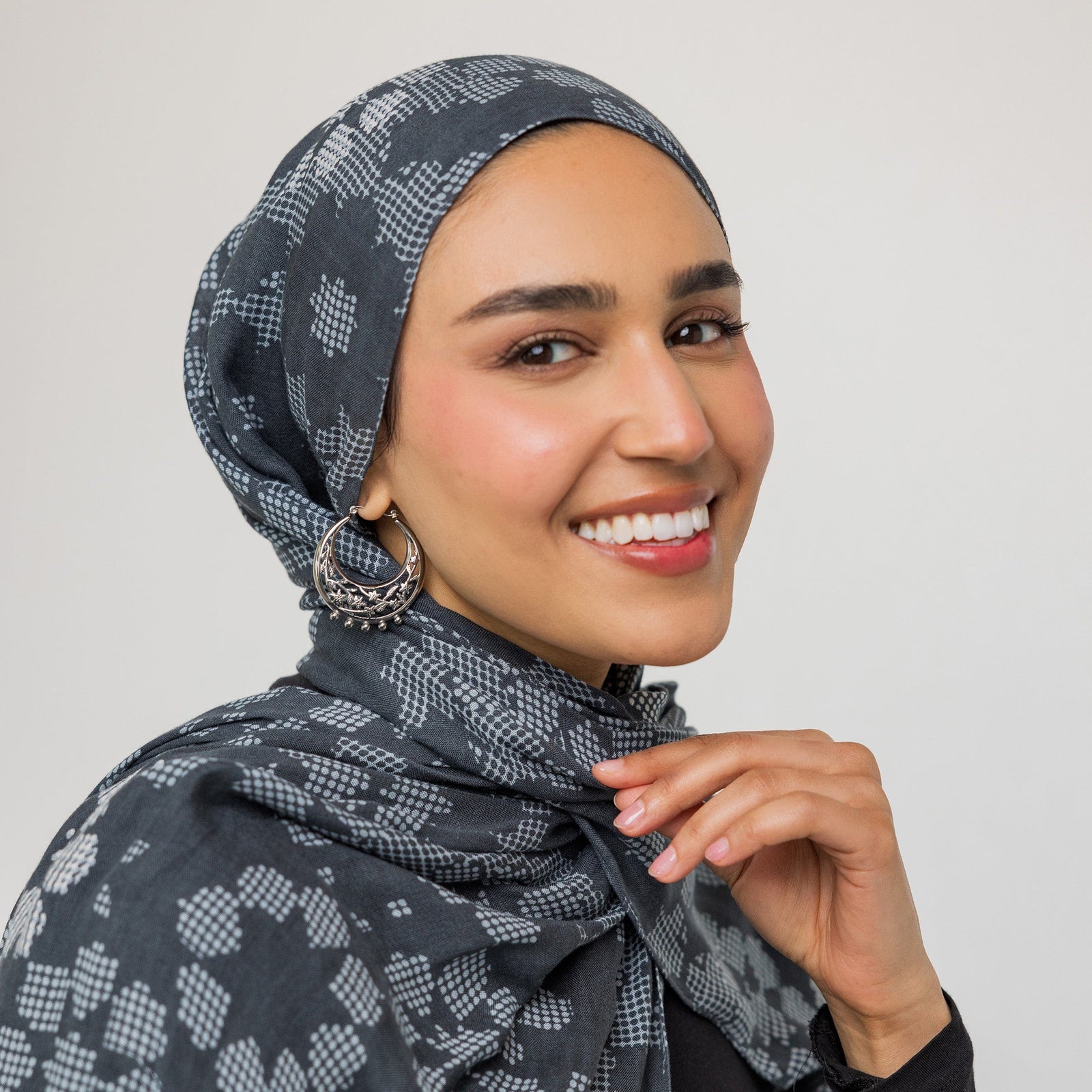 A female model with light skin tone showcasing the silver Jasmine Crescent Hoop Earrings. The earrings hang gracefully, enhancing her simple attire and drawing attention to the detailed crescent and jasmine vine motif.