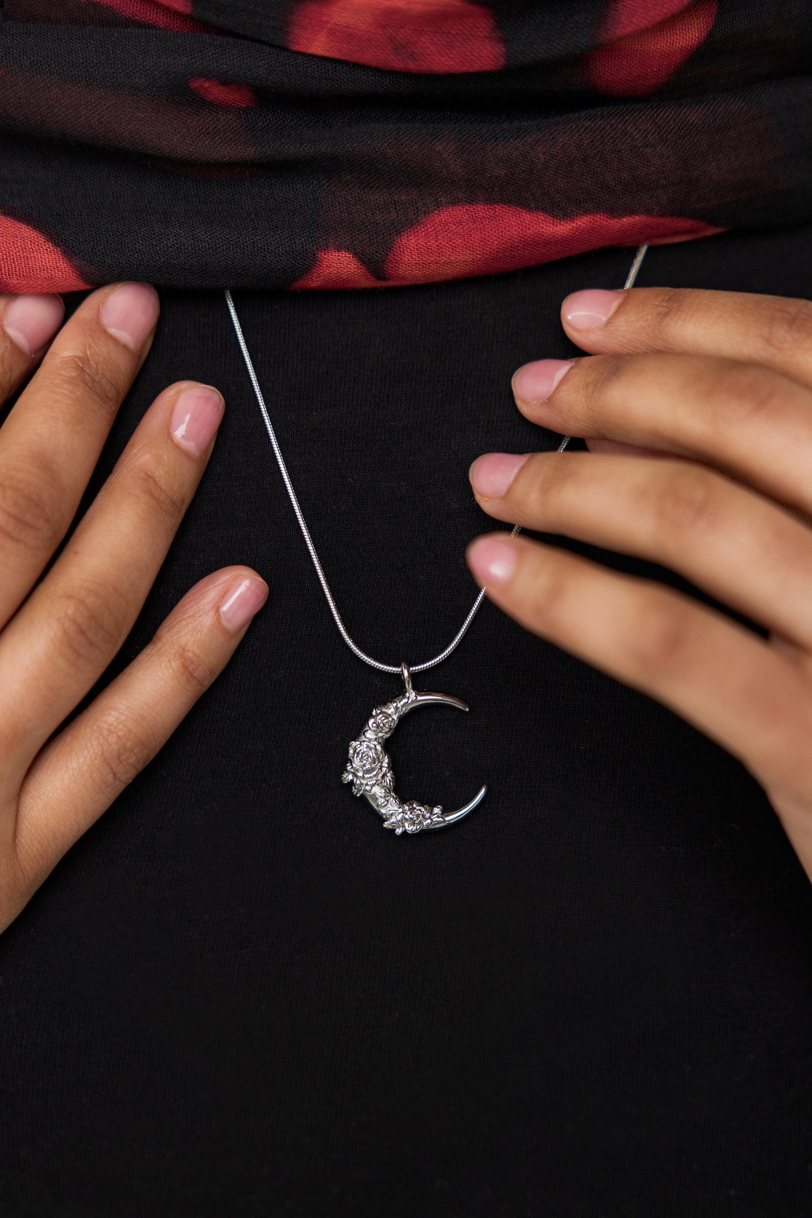 A model wearing the Damask Rose Crescent Necklace at its full 22-inch length. The necklace rests gracefully on the collarbone, highlighting the crescent moon pendant with rose detailing against a simple, neutral-toned outfit.