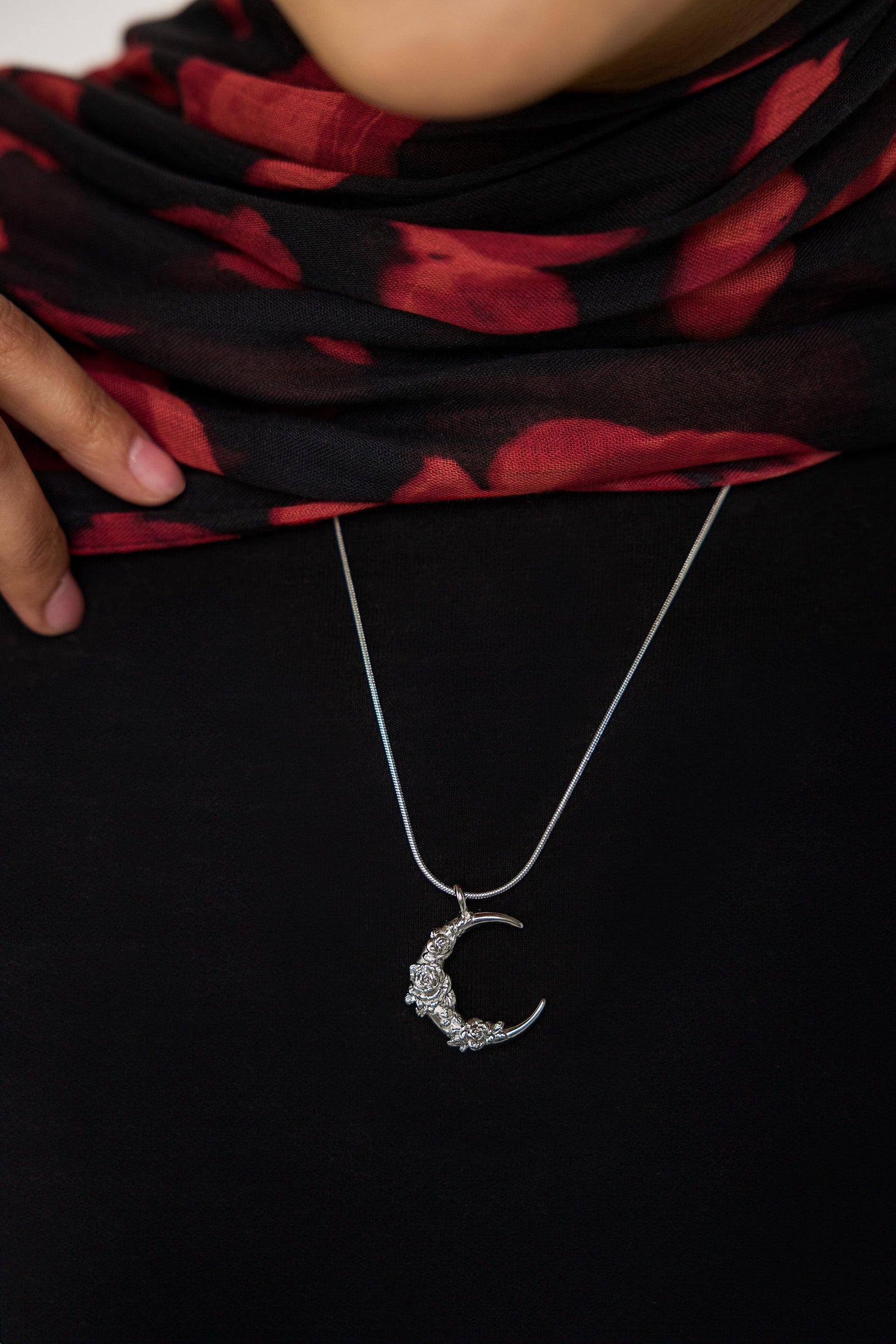 A model wearing the Damask Rose Crescent Necklace at its full 22-inch length. The necklace rests gracefully on the collarbone, highlighting the crescent moon pendant with rose detailing against a simple, neutral-toned outfit.