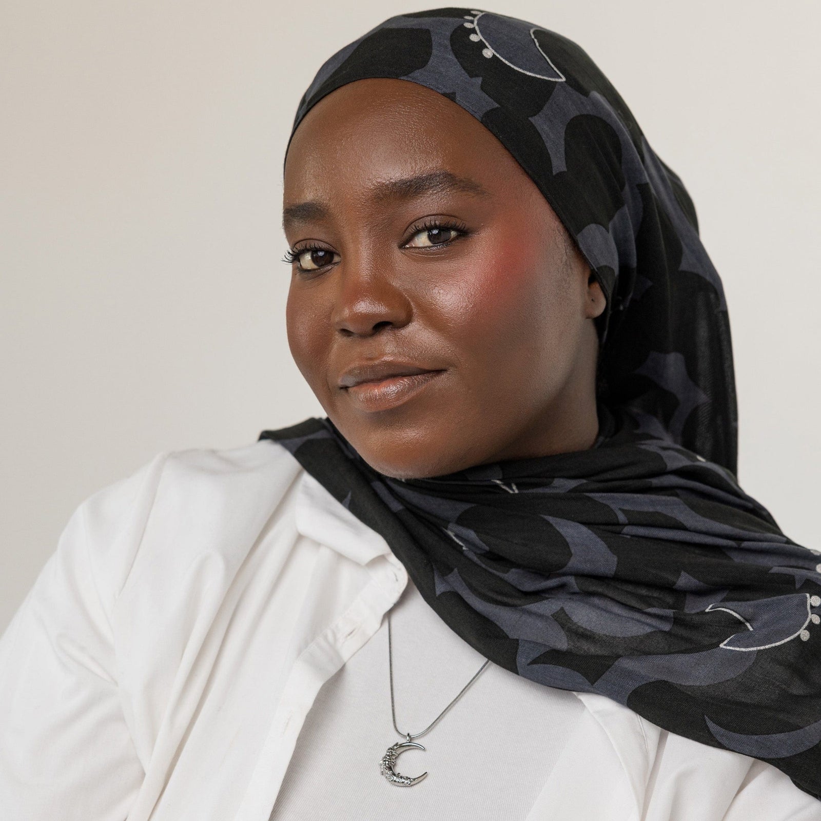 A female model with dark skin tone showcasing the silver Jasmine Crescent Necklace. The intricately designed crescent pendant hangs gracefully from the Harmony Chain, enhancing her neckline.