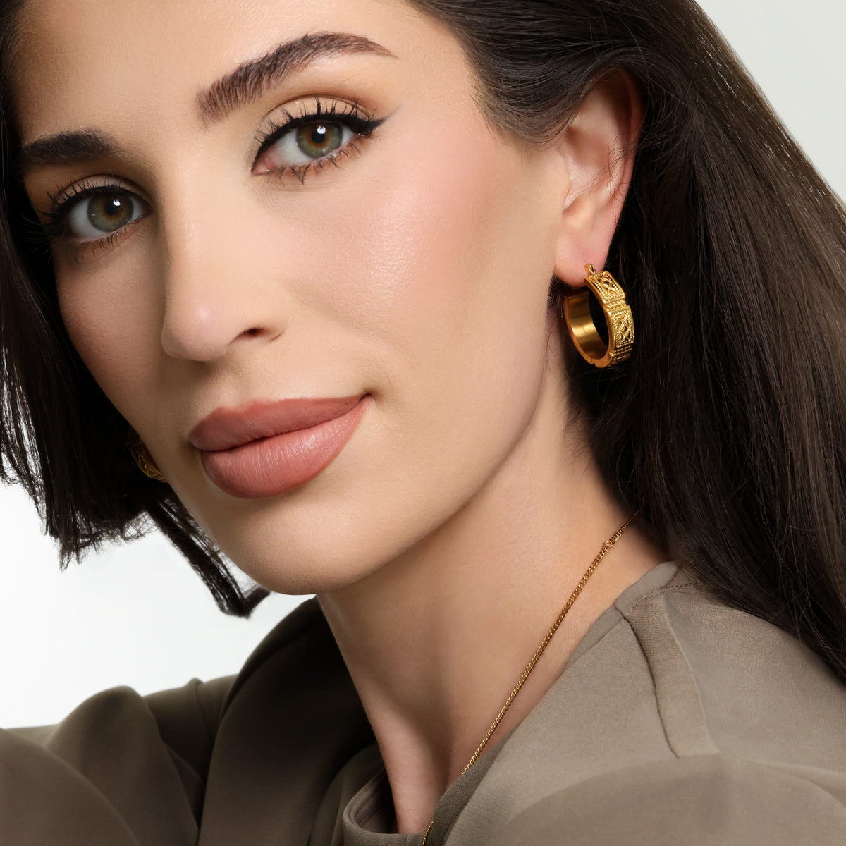 Photo of the model wearing the gold Damascus Tile Earring on their left ear.