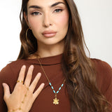 Woman wearing an 18k gold plated necklace with a sculpted daffodil flower pendant and turquoise blue tube beads, paired with gold hoop earrings and a bracelet