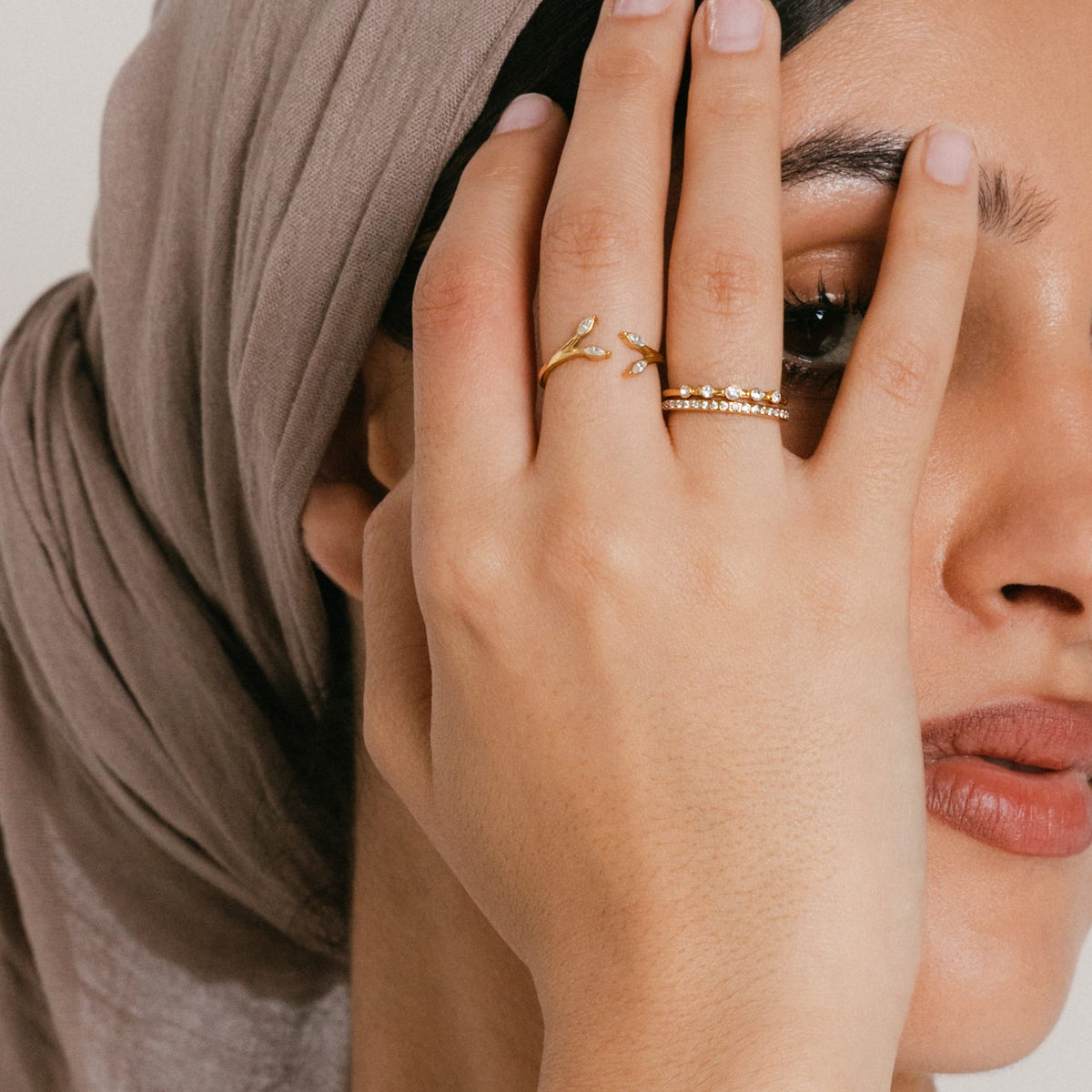 Model wearing a ring stack featuring an 18k gold-plated Five-Stone Bezel Band stacked above a Bezel Band on the index finger, and an Olive Branch Marquise Bezel Ring on the middle finger.