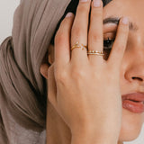 Model wearing a ring stack featuring an 18k gold-plated Five-Stone Bezel Band stacked above a Bezel Band on the index finger, and an Olive Branch Marquise Bezel Ring on the middle finger.