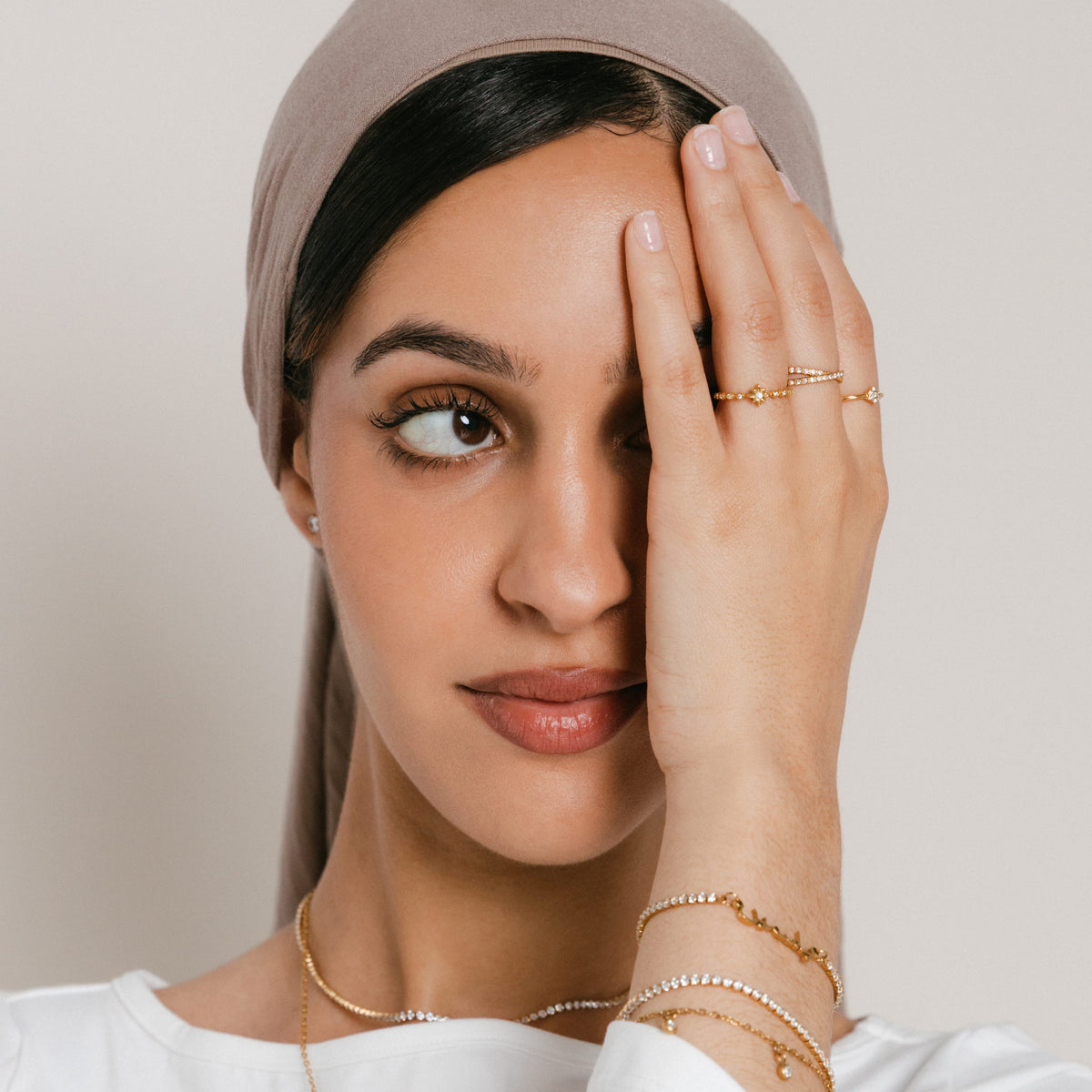 Model wearing a jewelry look featuring 18k gold-plated pieces: the North Star Bezel Ring on the index finger, Intertwined Bezel Ring on the middle finger, and Mughal Bloom Bezel Ring on the ring finger, paired with a Tennis Name Bracelet with custom Arabic calligraphy and layered pavé crystal bracelets.