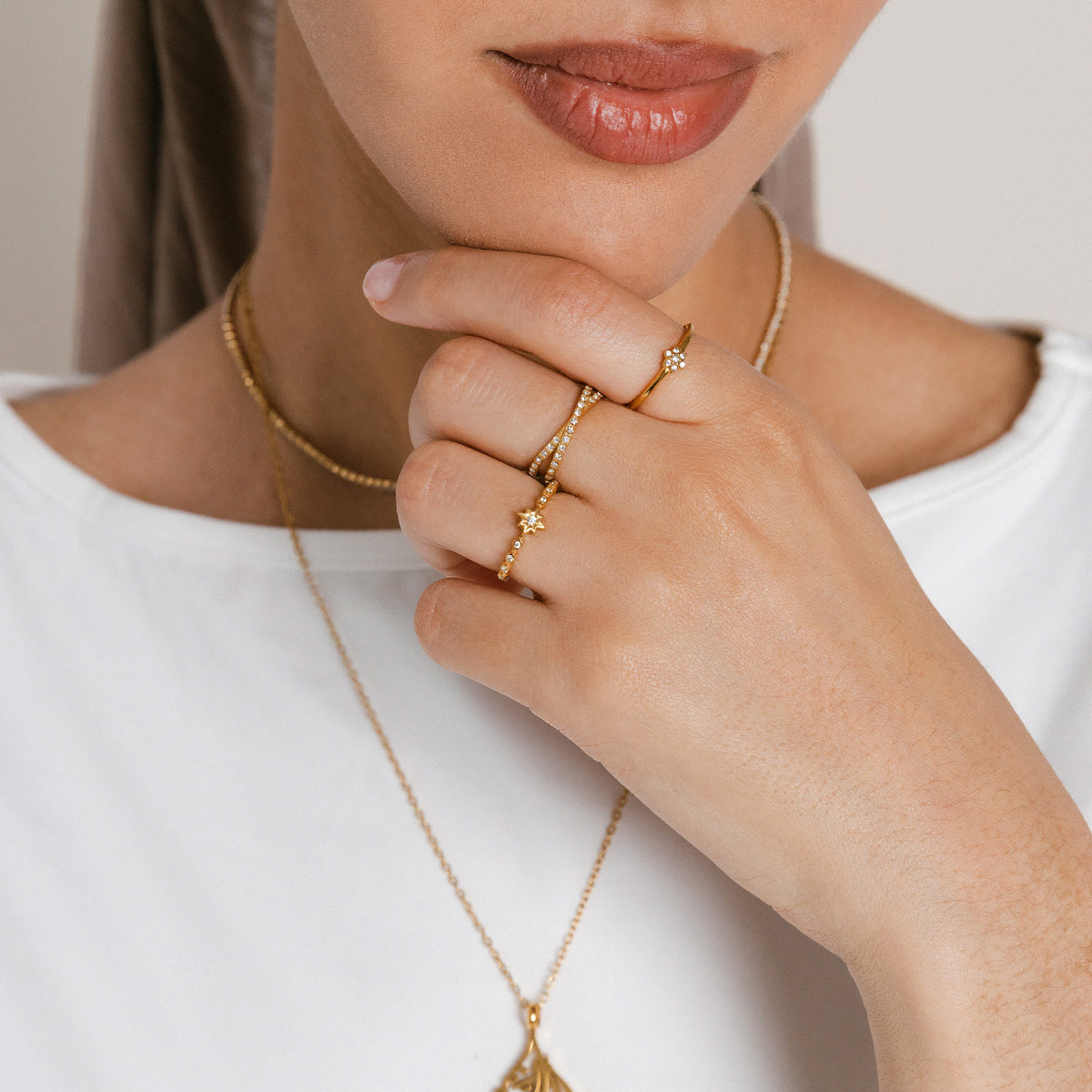 Model wearing an 18k gold-plated ring stack featuring the Mughal Bloom Bezel Ring on the index finger, Intertwined Bezel Ring on the middle finger, and North Star Bezel Ring on the ring finger, paired with layered gold necklaces.