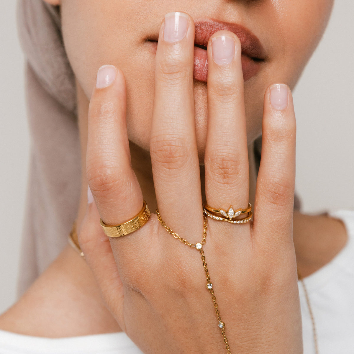 Model wearing 18k gold-plated jewelry featuring an engraved gold band ring on the index finger, a hand chain with bezel-set clear crystals anchored on the middle finger, and a Triple Marquise Bezel Ring stacked above an Intertwined Bezel Ring on the ring finger.