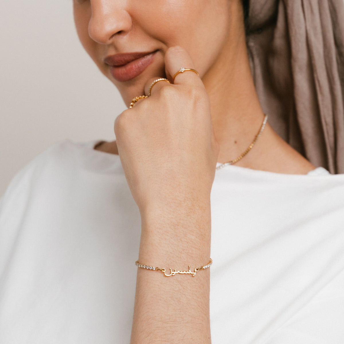 Model wearing 18k gold-plated jewelry featuring a Tennis Name Bracelet with custom Arabic calligraphy, paired with a ring stack featuring the Mughal Bloom Bezel Ring on the index finger, Intertwined Bezel Ring on the middle finger, and North Star Bezel Ring on the ring finger.