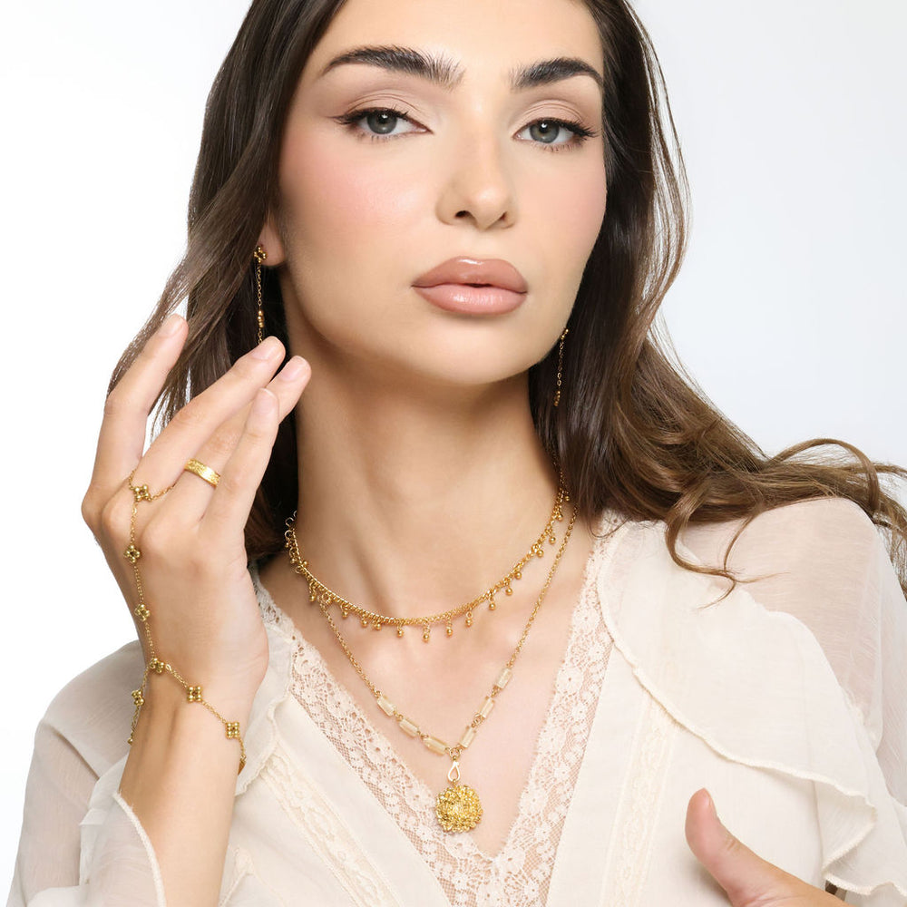 Woman wearing an 18k gold plated layered necklace with a chrysanthemum flower pendant featuring a bright blue enamel center and pale yellow tube beads