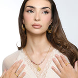 Woman wearing an 18k gold plated necklace with a textured gold flower pendant and pink and black marbled tube beads, paired with ornate gold hoop earrings