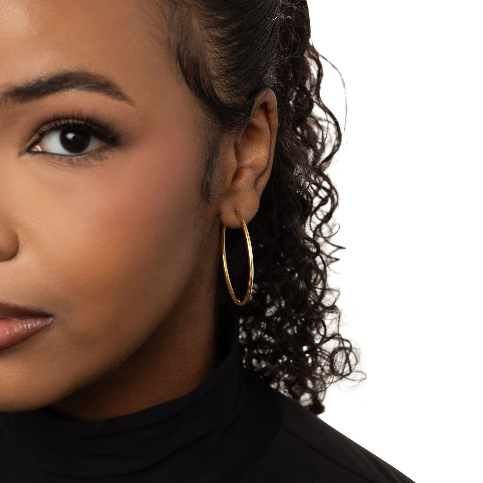 Photo of the left side of the model's face. The model is wearing the gold Oversized Essential Hoops | 40mm on their left ear.