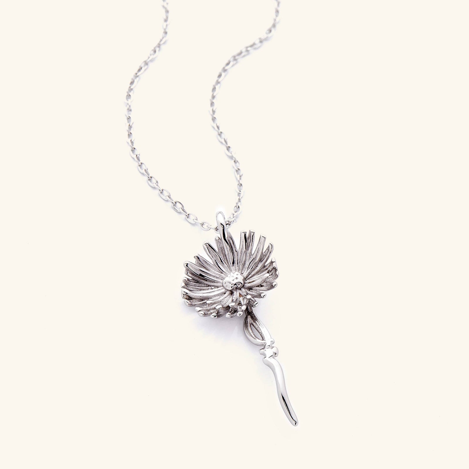 A silver necklace with the aster flower shaped pendant that features  Arabic word for ‘patience’, curving in calligraphy out of the stem of the flower.