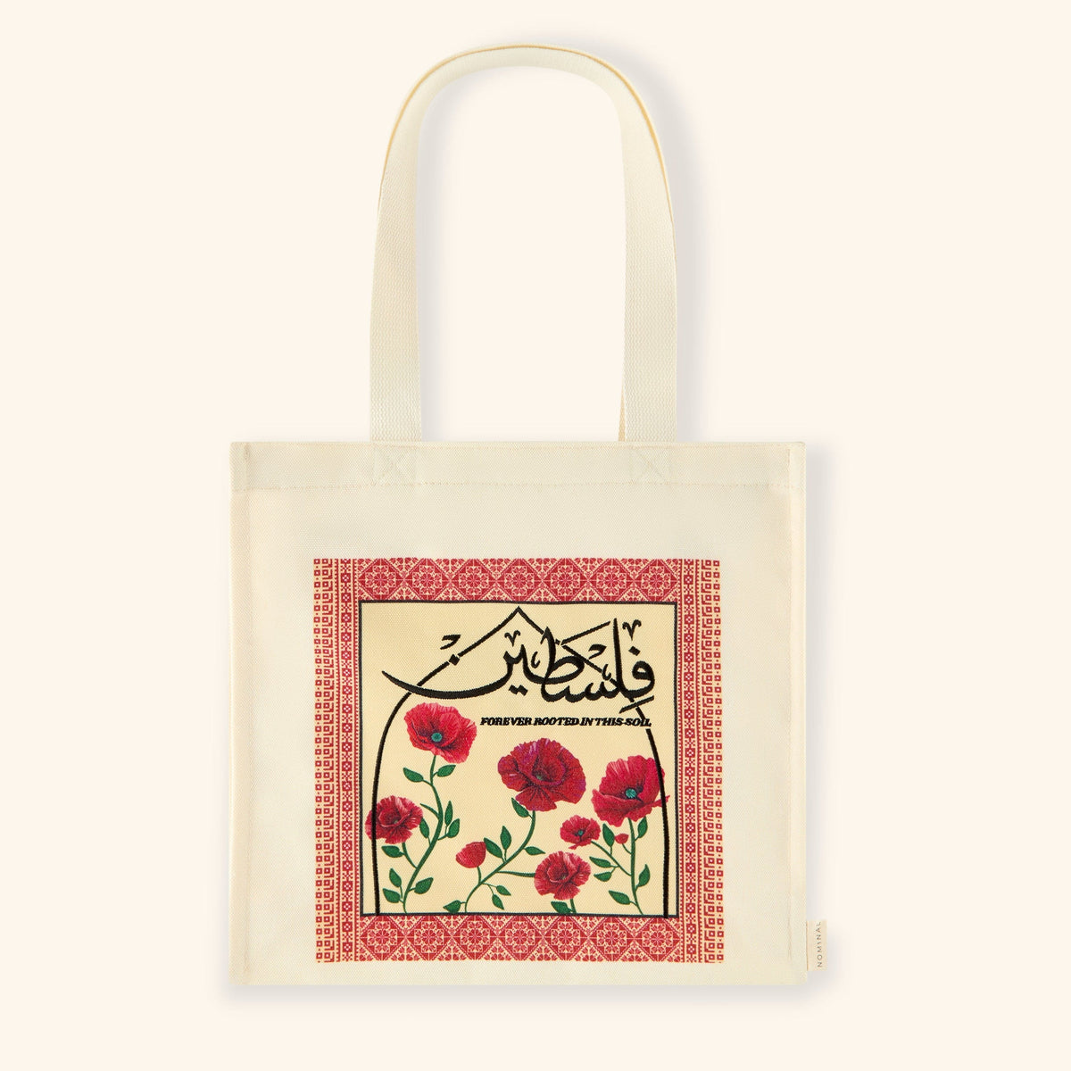Cream-colored canvas Poppy Tatreez Palestine tote featuring a bold embroidered panel. The design includes red poppy flowers and Arabic calligraphy reading “Filasteen” with English text below that says “Forever rooted in this soil,” all framed with a red tatreez-style border.
