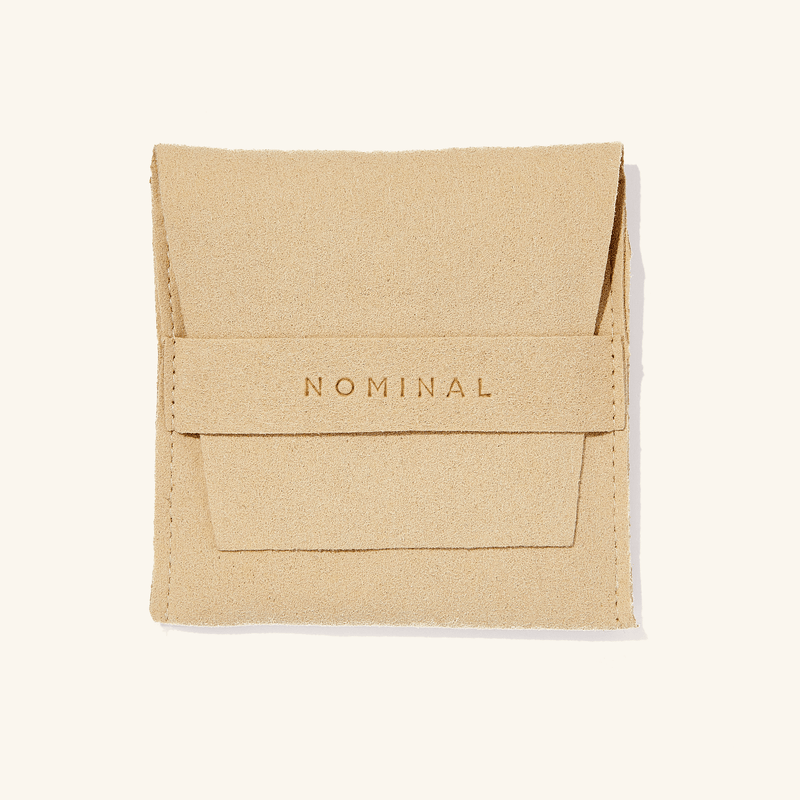 Beige suede jewelry pouch with 'NOMINAL' pressed in lettering on the front flap strap pimage_ flat against a light background.