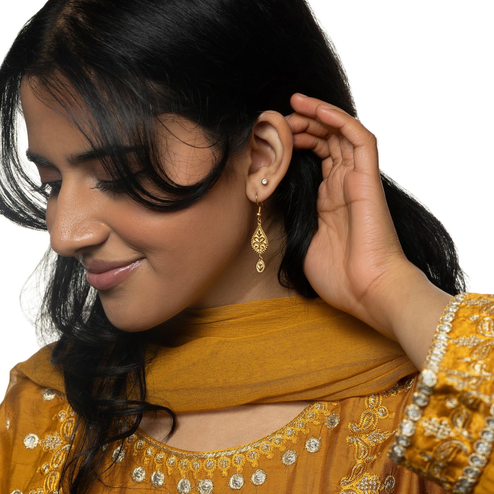 Model moves their hair with their left hand. Model is wearing the gold Paisley Garden Earrings on their left ear.